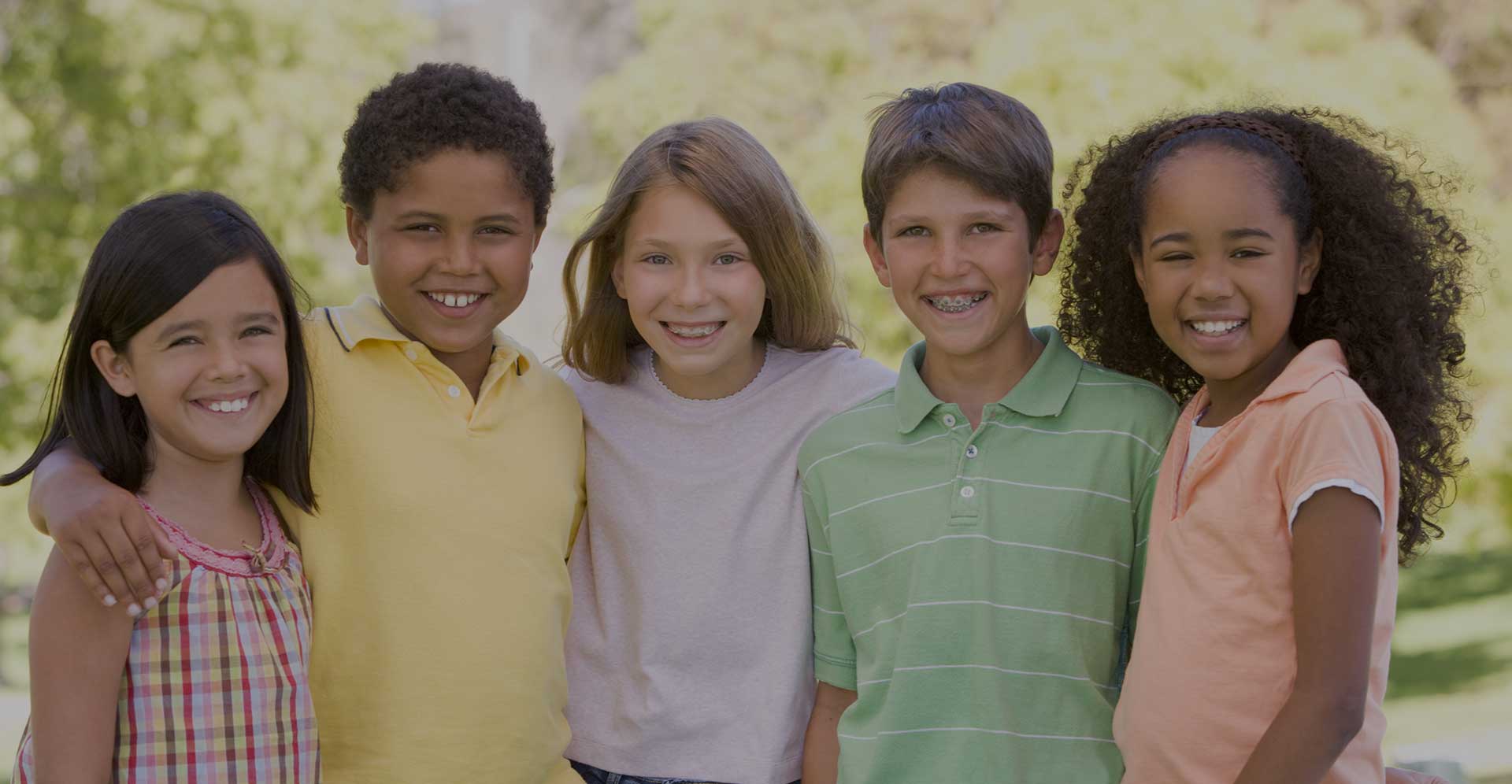 Five children standing in a row in a park smiling at camera